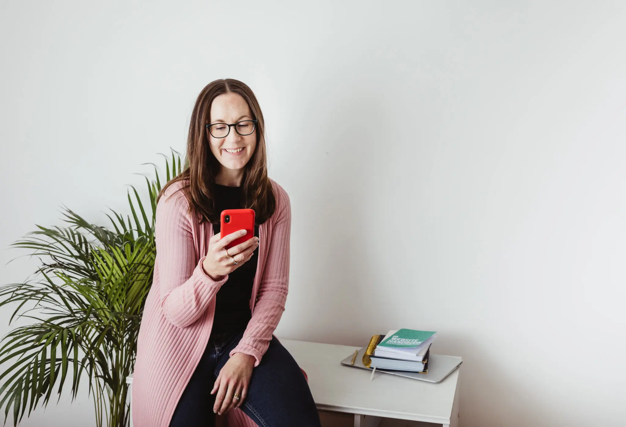 Jude sitting on a desk looking at her phone during a brand photos shoot