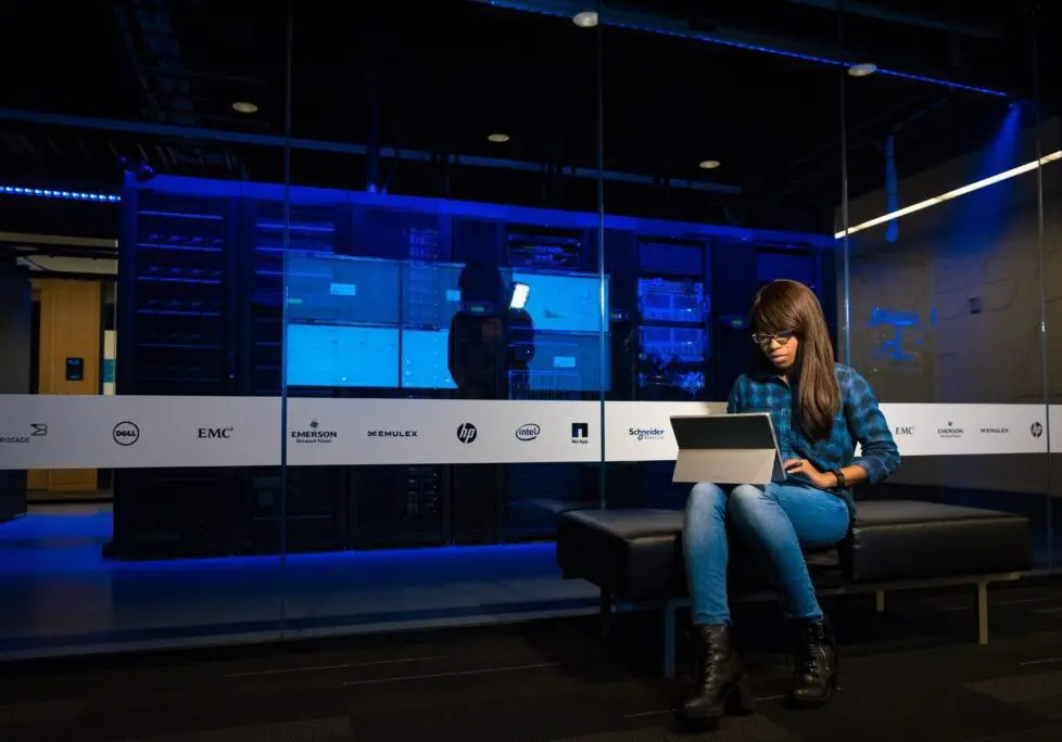 Woman on laptop sitting in a server room used for web hosting
