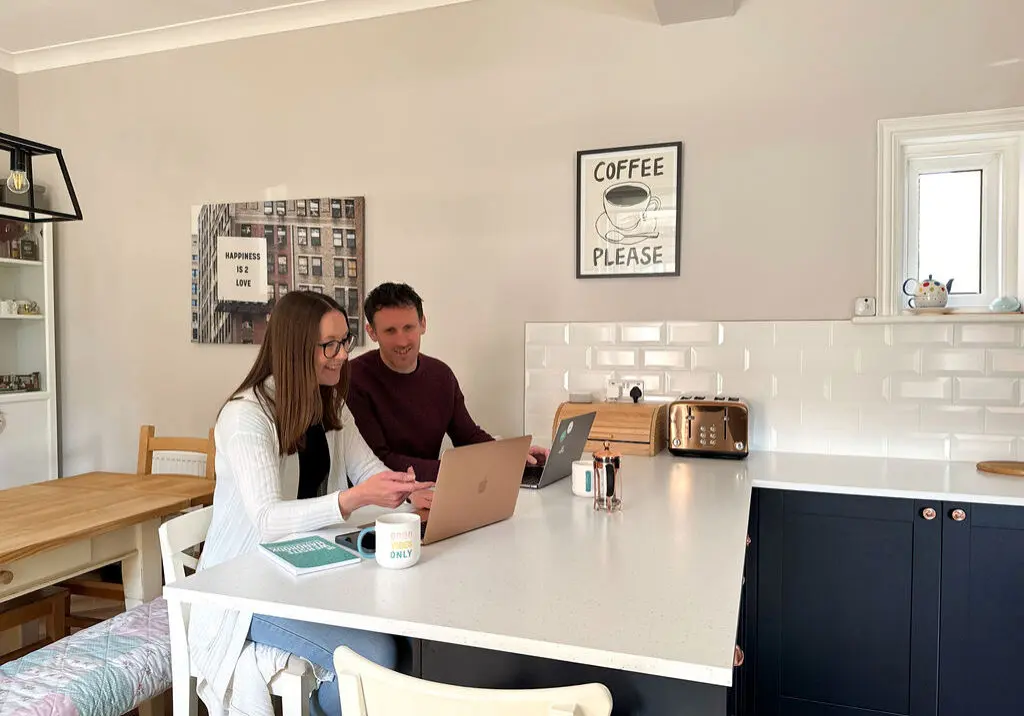 Chris and Jude happy working at laptops in the kitchen.