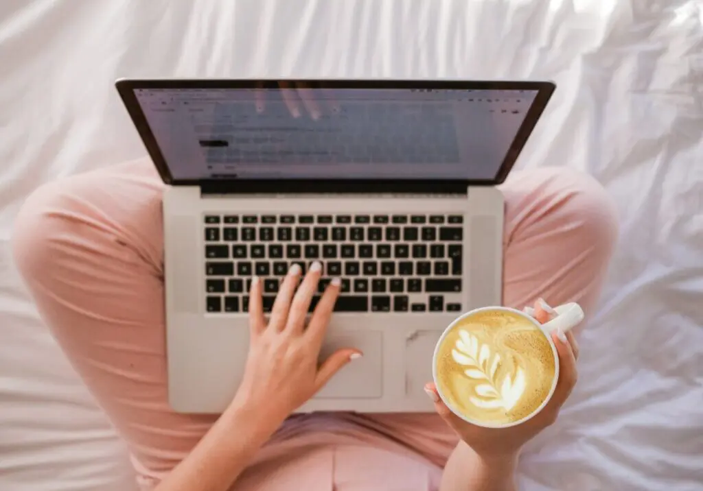 Laptop on woman's lap with a blog post on the screen. She's also holding a coffee.