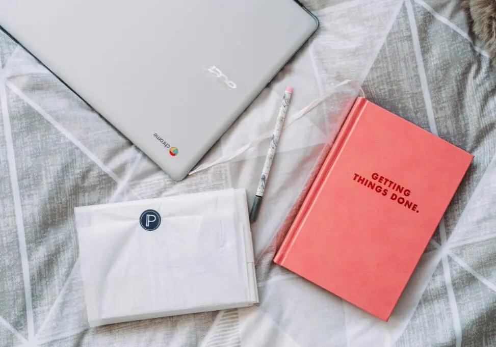 Laptop and notebook on bed of person trying to get more done