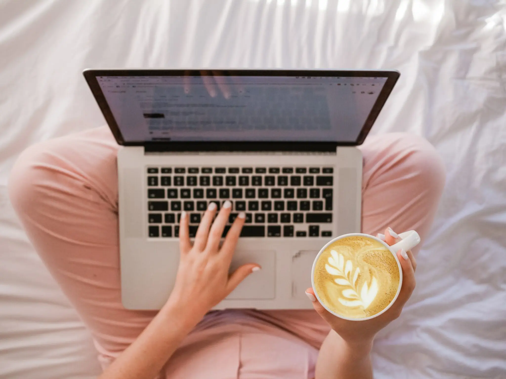Laptop on woman's lap with a blog post on the screen. She's also holding a coffee.