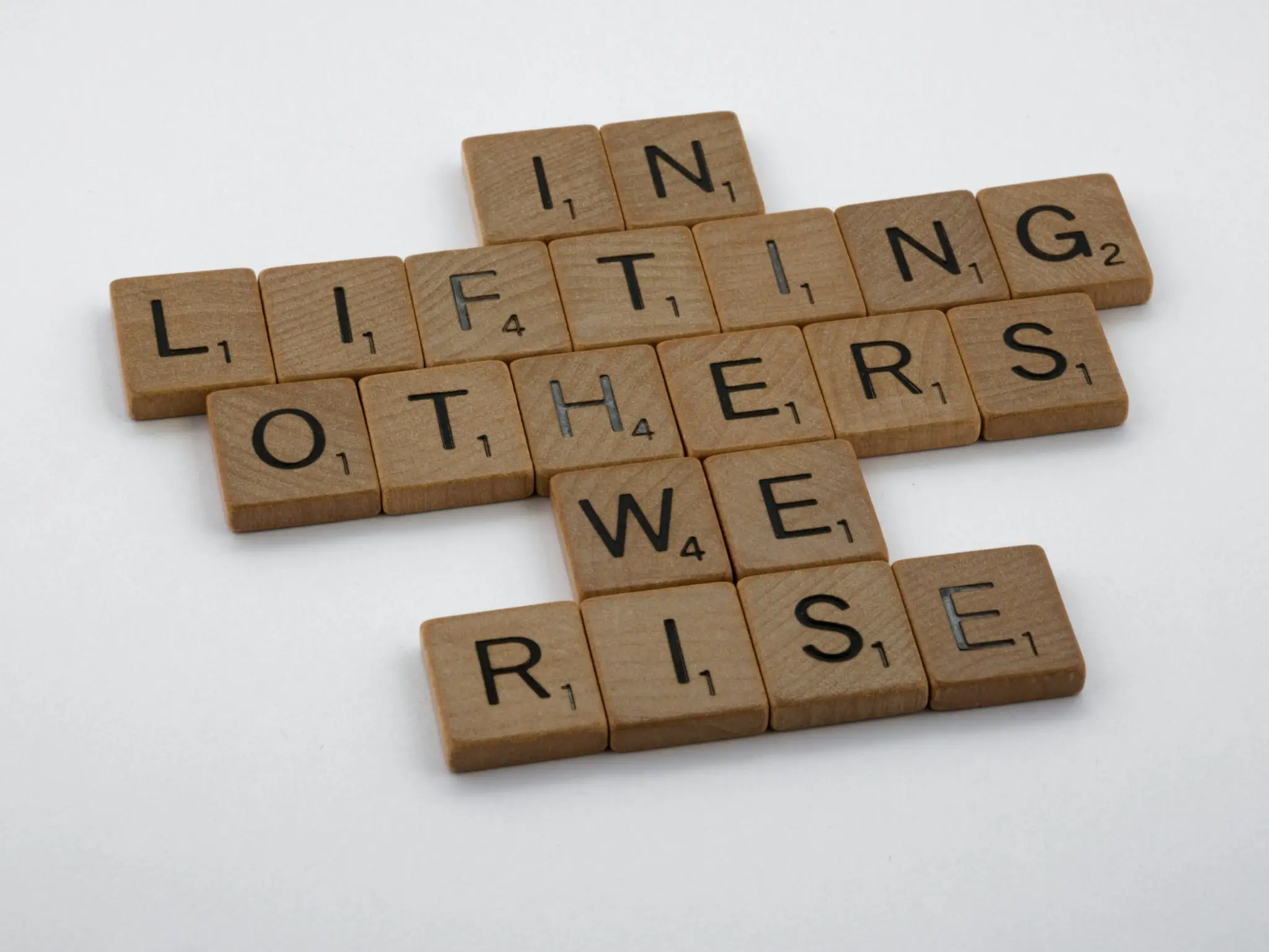 In Lifting Others We Rise made out of wooden scrabble tiles
