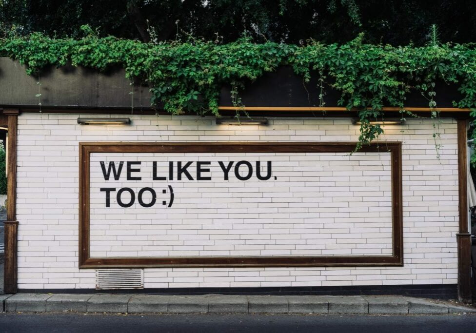 "We like you too :)" written on a white metro tile style wall outside