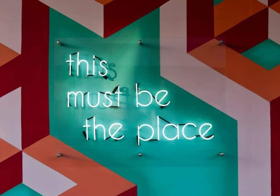 "This must be the place" written in lights on an artistic modernist patterned wall