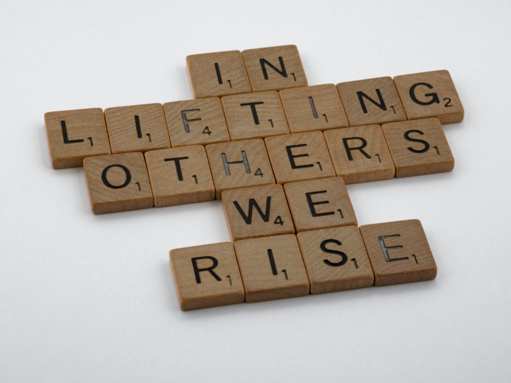 In Lifting Others We Rise made out of wooden scrabble tiles