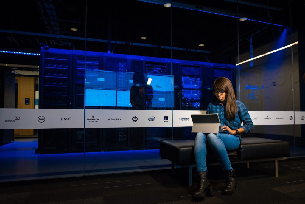 Woman on laptop sitting in a server room used for web hosting