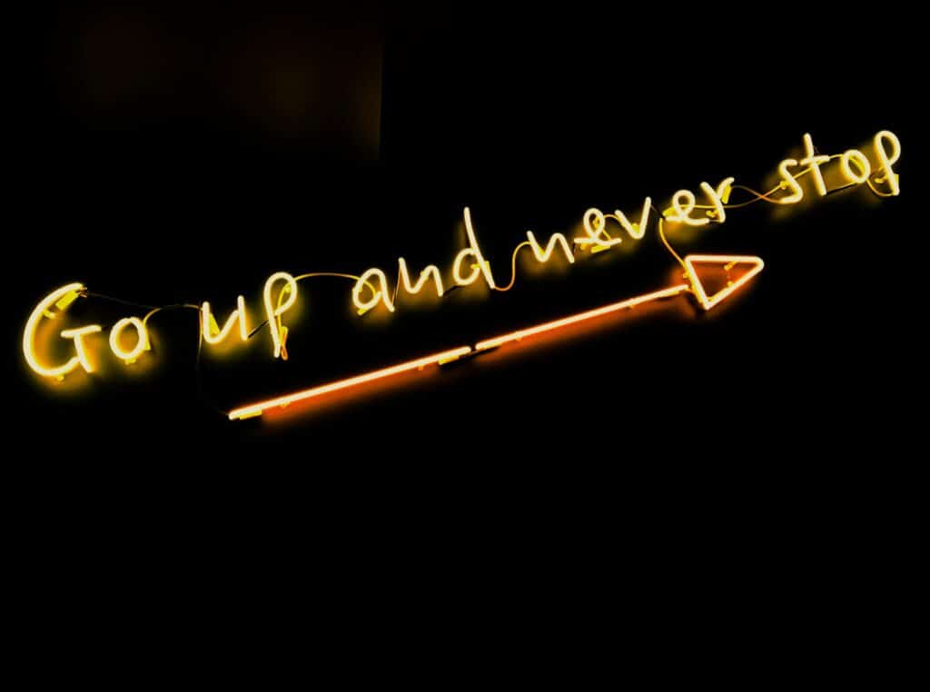 neon words saying go up and never stop with an arrow underneath slanting up